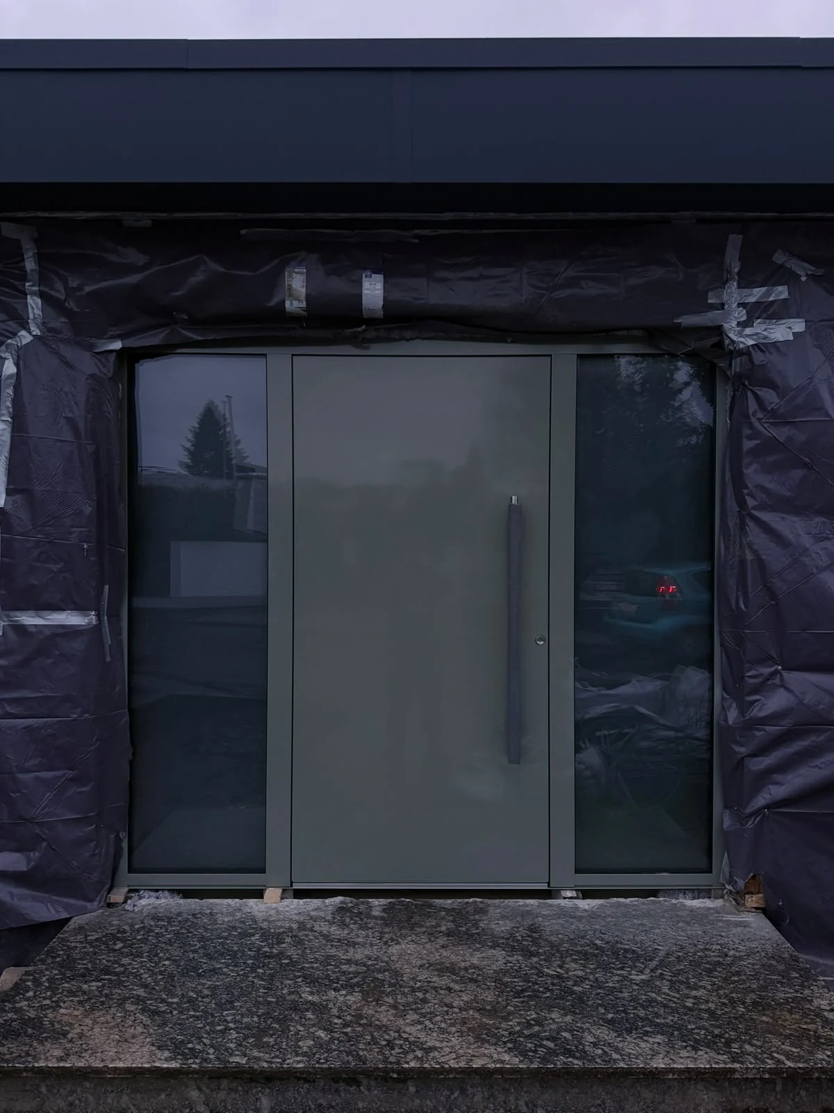 Frontansicht der grünen Haustür mit zwei verglasten Seitenteilen.